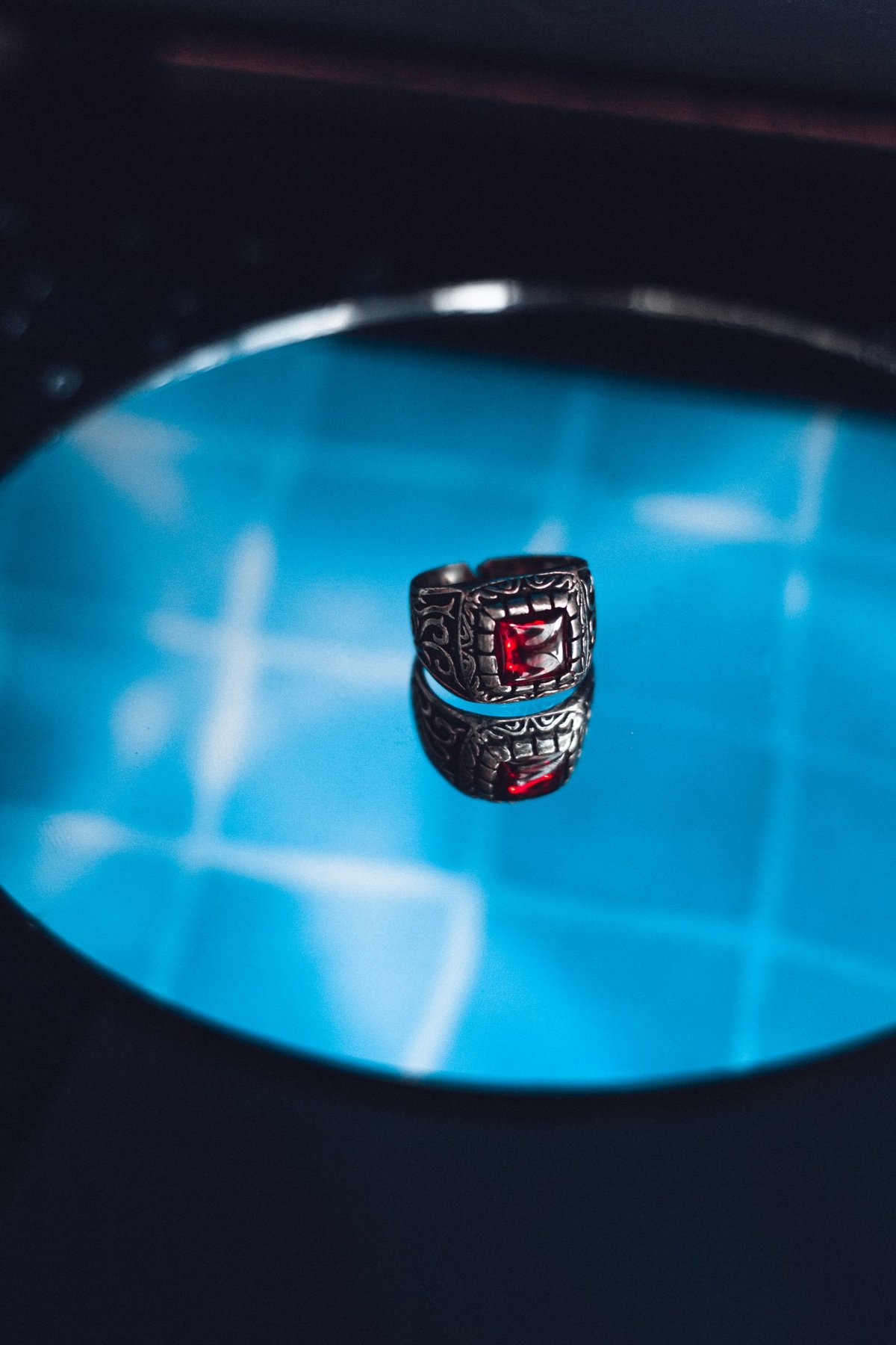 A red-stone ring on a reflective surface.