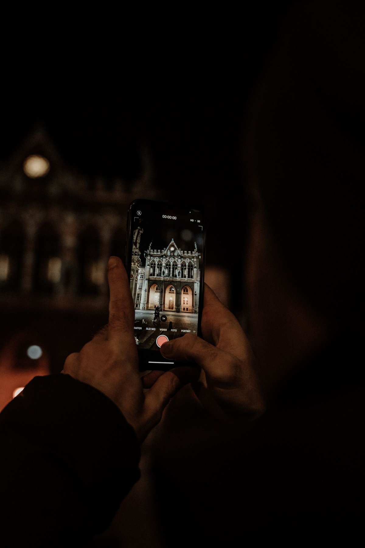 A smartphone photographs an illuminated building at night.